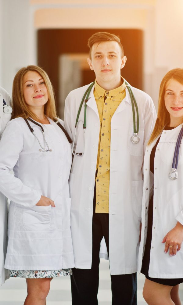 Group of young doctors in white coats posing in the hospital.